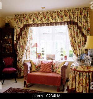 Piccolo divano nella parte anteriore della finestra con motivi floreali e tende mantovane di corrispondenza Foto Stock