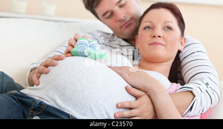 Carino futura mamma giacente con mio marito sul divano azienda scarpe per bambini Foto Stock