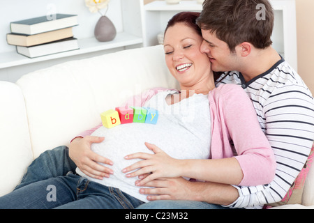Ritratto di un felice donna incinta con cubetti di bambino sul suo ventre e di suo marito la bacia su una Foto Stock