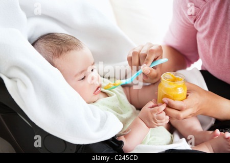 Close-up di una giovane madre dando purea di carota al suo bambino per il pranzo nel soggiorno Foto Stock