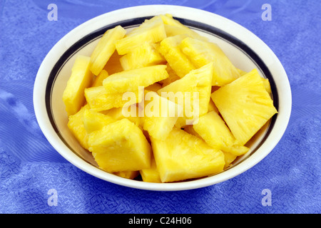 Pezzi di esotico giallo maturi frutti d'oro in una vaschetta di colore bianco con un grazioso sfondo blu. Giallo dolce di ananas in pezzi in una ciotola rotonda su un luogo mat Foto Stock