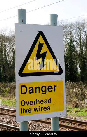 Pericolo cavi aerei sotto tensione segnale di avvertimento a fianco della linea ferroviaria, Harston, Cambridgeshire, England, Regno Unito Foto Stock