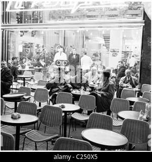 1950s. Presto la sera e giovani uomini parigino seduti in sedie di vimini gustando un drink e discussione insieme al di fuori di un cafe bar, Parigi, Francia. Foto Stock