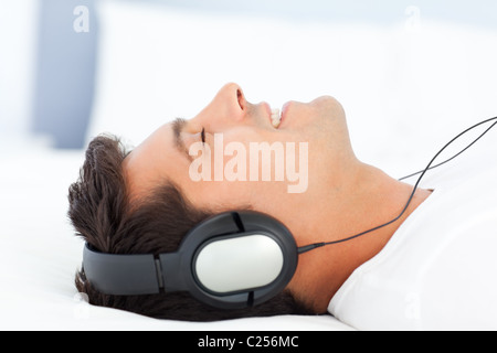 Uomo gioioso ascolto di musica sdraiato sul suo letto Foto Stock