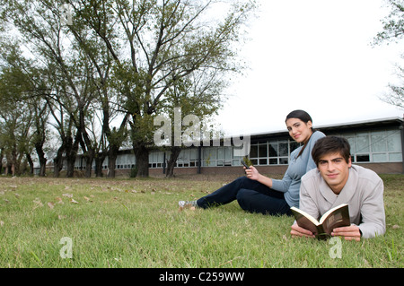 Gli studenti universitari che giace sul campo guardando un telefono cellulare e la lettura di un libro Foto Stock