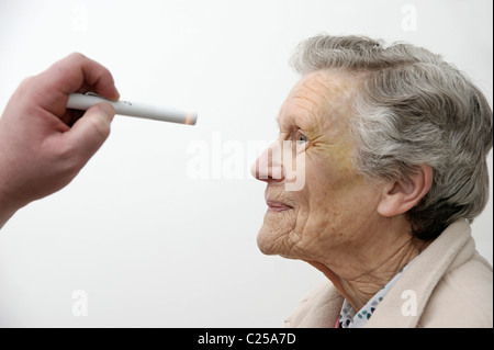 Medico controllo dell'occhio per la dilatazione della pupilla dopo un incidente / caduta di una donna anziana Foto Stock