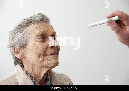 Medico controllo dell'occhio per la dilatazione della pupilla dopo un incidente / caduta di una donna anziana Foto Stock