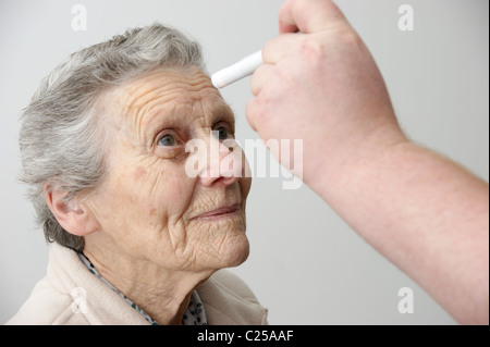 Medico controllo dell'occhio per la dilatazione della pupilla dopo un incidente / caduta di una donna anziana Foto Stock