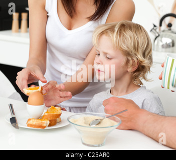 Madre attenta la rottura di un uovo sodo per suo figlio durante la prima colazione Foto Stock