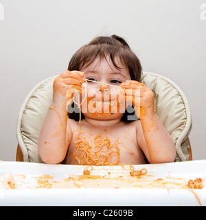 Happy baby divertirsi mangiando sudicie coperte in spaghetti azienda Angel Hair Pasta marinara rosso salsa di pomodoro. Foto Stock