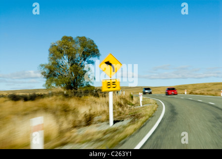 Motion Blur effetto - curva a sinistra, 85 km/h velocità segno consultivo. Rosso e argento auto che si avvicinano. Foto Stock