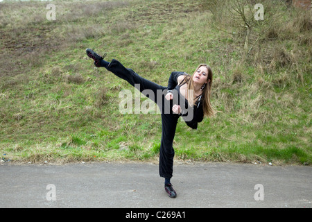 Giovane donna caucasica facendo un tae kwon do kick esterno, preso in Emersons Green, Bristol Foto Stock