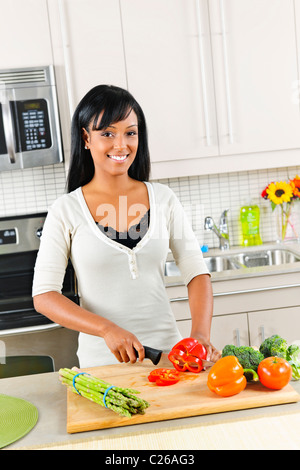 Sorridente donna nera come tagliare le verdure in cucina moderna interno Foto Stock