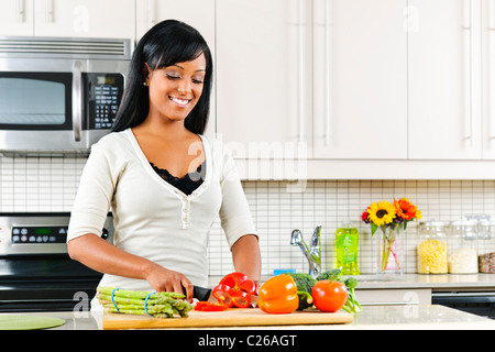Sorridente donna nera come tagliare le verdure in cucina moderna interno Foto Stock