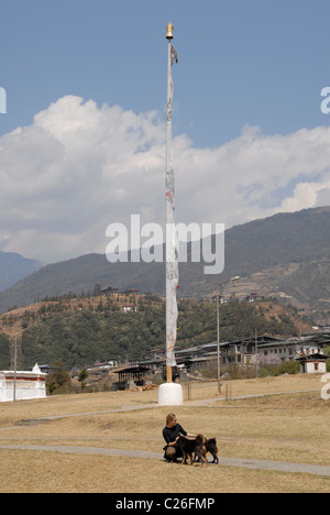 Donna con 2 cani nella parte anteriore di una bandiera di preghiera, Chorten Kora, Trashiyangtse, Est Bhutan Foto Stock