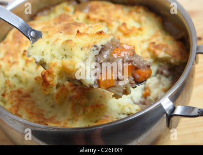Un cucchiaio pieno di pastore pie (carni macinate e stufato di verdura conditi con purè di patate) sopra il recipiente di cottura. Foto Stock