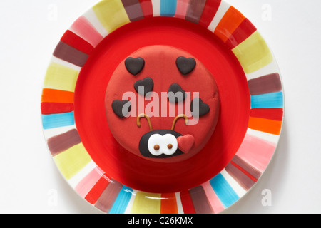 Torta di marzapane in forma di una coccinella lady bird collocato sulla colorata targhetta rossa Foto Stock