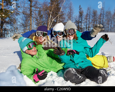 Ritratto di quattro ridere gli adolescenti nelle maschere da sci seduti sulla neve Foto Stock