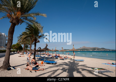 I turisti a prendere il sole sotto le palme sulla spiaggia presso la bella spagnolo resort di Puerto de Alcudia Foto Stock