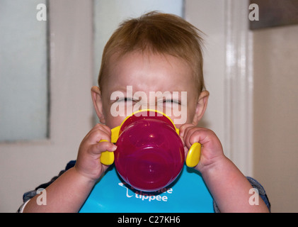 Baby boy bere dal bicchiere evolutivo Foto Stock