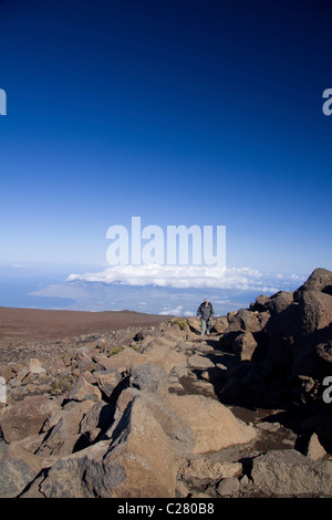 L'uomo escursionismo in prossimità della sommità di 10.000 piedi Vulcano Haleakala a Maui. West Maui può essere visto a distanza. Foto Stock