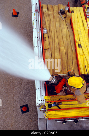 Vista dall'alto in basso sul vigile del fuoco la spruzzatura di acqua da un tubo montato su di un camion dei pompieri Foto Stock