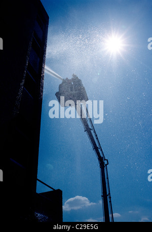 Vigile del fuoco la spruzzatura di acqua da un tubo montato su una scala bucket di un camion dei pompieri Foto Stock