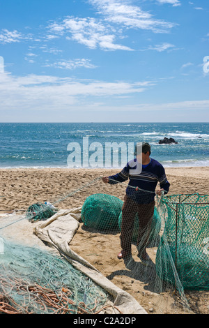 Pescatore portoghese esaminando le reti sulla riva Foto Stock