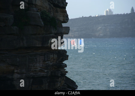 Due barche a vela racing passato una rupe a bordo nel porto di Sydney Foto Stock