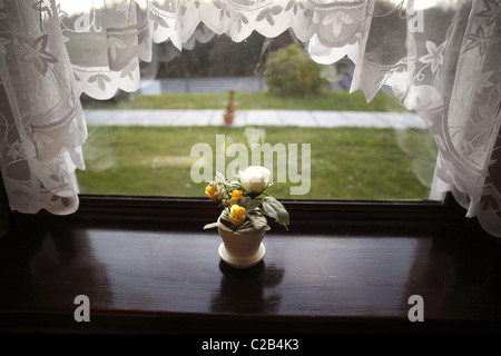 I fiori di plastica sul davanzale incorniciato da tendine. Foto Stock