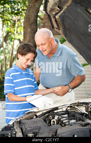 Padre insegnando il suo giovane figlio per controllare il livello di olio nell'auto. Foto Stock