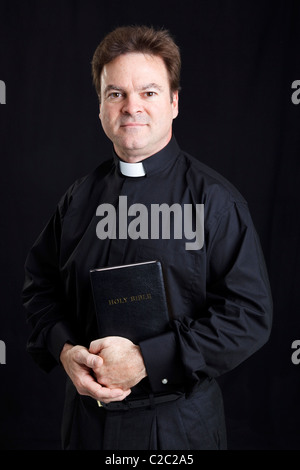 Ritratto di un prete cattolico tenendo la bibbia. Sfondo nero. Foto Stock