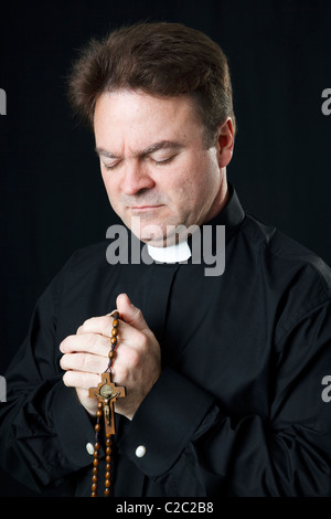 Sacerdote cattolico di pregare con il suo rosario. Foto Stock