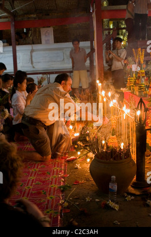 Le persone sono raccolte con le candele per rendere omaggio al Pra Bang Buddha in un tempio buddista in Laos comunista. Foto Stock