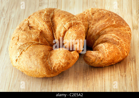 Due yummy sfaldabile appena sfornato grano intero croissant su bambù tagliere pronto per essere servito. Foto Stock