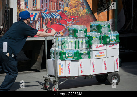 Consegna uomo spinge un carrello con la Polonia acqua sorgiva e altre forniture per ufficio da W.B. Mason Foto Stock