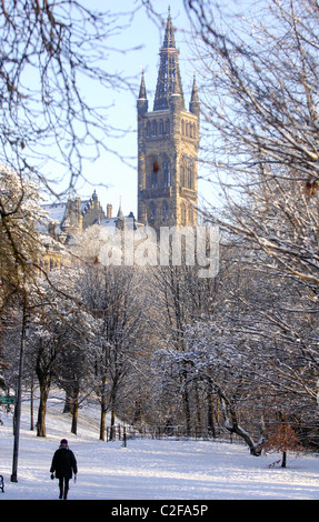 Una persona che cammina attraverso il Kelvingrove Park a Glasgow dopo una nevicata. L'Università di Glasgow è raffigurato dietro. Foto Stock