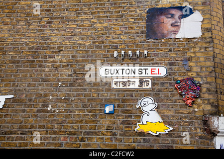 Graffiti o di arte di strada sulla parete con il nome della strada segno ed equivalenti in lingua bengalese, Buxton Street, Off Brick Lane, Londra, E1, Regno Unito Foto Stock