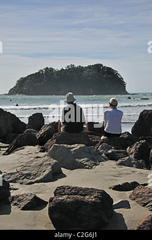 Coppia più anziana seduta su rocce sulla spiaggia, Monte Maunganui, Tauranga, Bay of Plenty Region, Isola del Nord, Nuova Zelanda Foto Stock