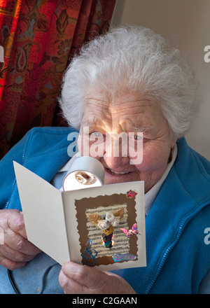 Felice 90's senior independent anziana signora con una lente di ingrandimento da lettura gode di una artigianale di biglietto di auguri nella sua casa soggiorno Foto Stock