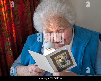 Anziani compleanno card saluti felice 90's senior anziana signora con una lente di ingrandimento da lettura gode di una artigianale di biglietto di auguri nella sua casa soggiorno Foto Stock