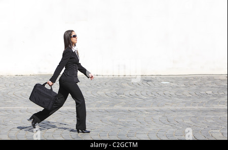 Giovane imprenditrice a piedi lungo una strada di ciottoli di fronte un muro bianco. Foto Stock
