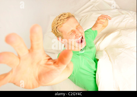 Giovani allegro uomo europeo nel suo letto stretching per il risveglio. Prospettiva del volume girato. Foto Stock
