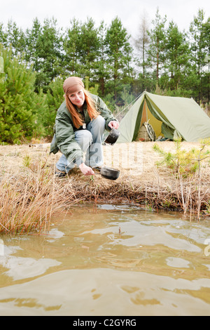 Tenda da campeggio donna felice lavaggio piatti nel flusso di acqua Foto Stock