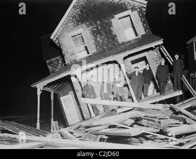 Gli uomini di stand sul portico di un mare luminoso Cottage strappato dalla sua fondazione ed inclinato di un angolo di 45 gradi. Foto Stock