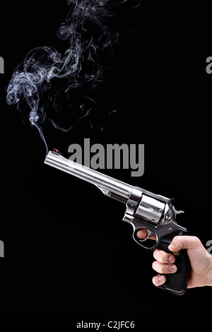 Mano che tiene un revolver con canna fumante, su sfondo nero Foto Stock