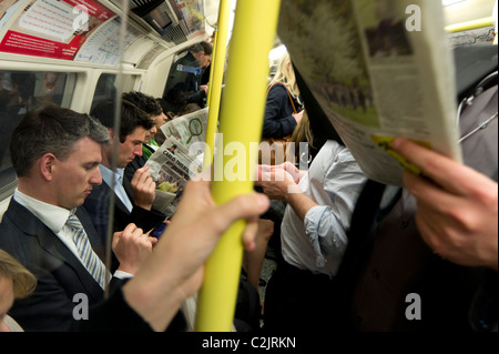 Passeggeri leggendo i giornali in un affollato Londra della metropolitana treno, London, England, Regno Unito Foto Stock