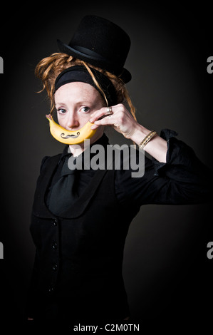 Giovani alt punky funky donna tenendo una banana con un baffi disegnato che oltre la sua bocca Foto Stock