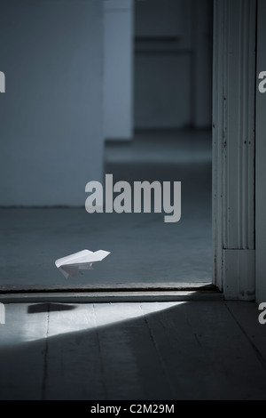 Un aeroplano di carta sta volando attraverso una porta momenti prima di atterrare sul pavimento Foto Stock