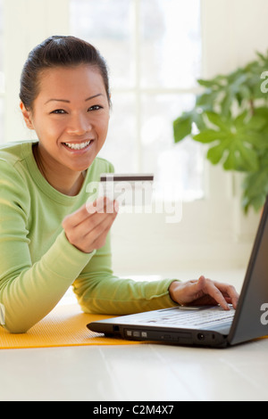 Sorridente giovane donna asiatica lo shopping online con carta di credito e il computer portatile Foto Stock